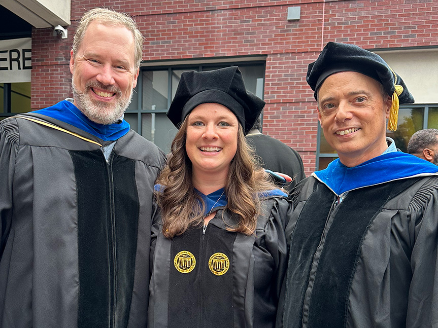 Bryce McLeod, Stephanie Violante and Micheal Southam-Gerow stand in front of a brick building wearing graduation regalia